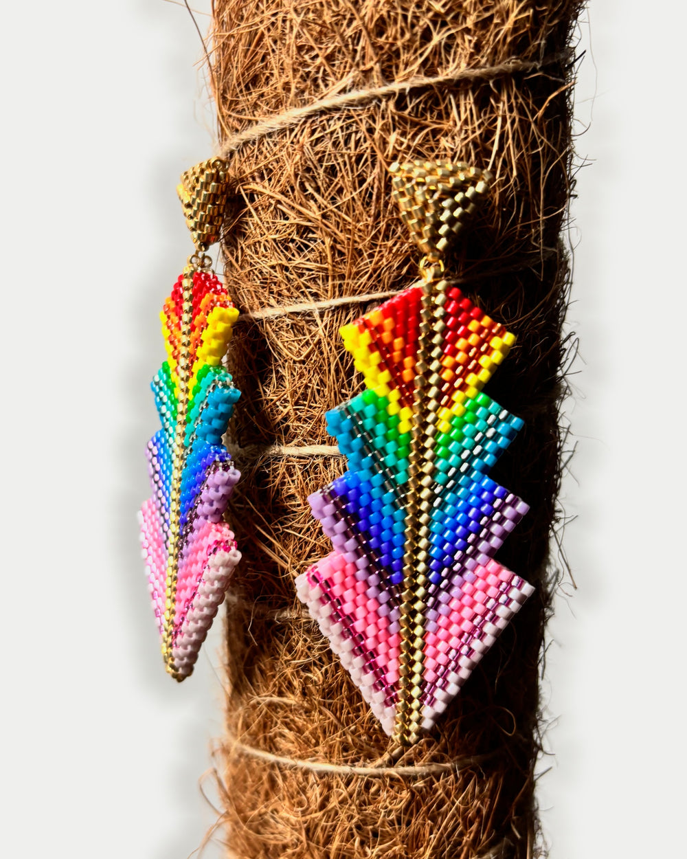 Fotografía real de los pendientes DAGIRA 001 sobre fibra de coco, con fondo exterior gris perla y encuadre centrado.